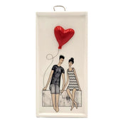 Ceramic white rectangular plaque with a seated couple painted on it holding a three dimensional red balloon