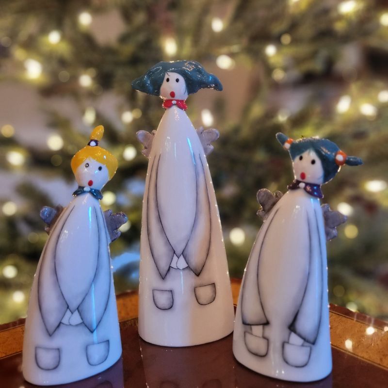 Trio of ceramic angels in front of a Christmas tree